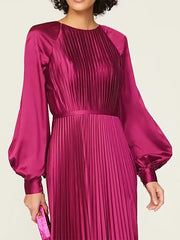 Woman wearing a magenta pleated dress with long sleeves on a plain background