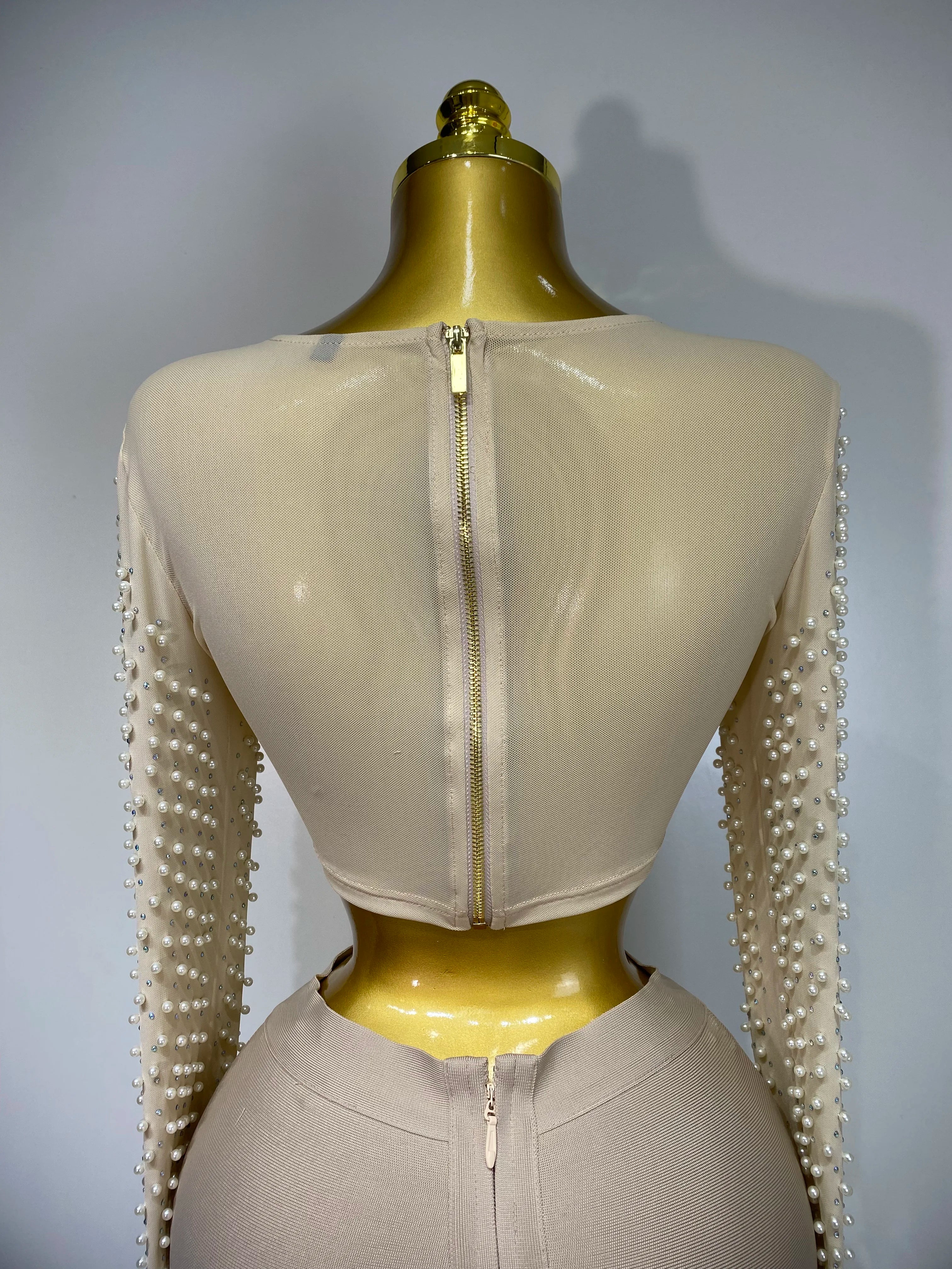 Mannequin wearing a beige outfit with pearl embellishments on sleeves against a gray background