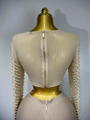 Mannequin wearing a beige outfit with pearl embellishments on sleeves against a gray background