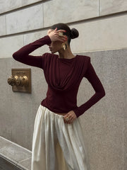 Woman wearing a burgundy top and white pants against a stone wall.