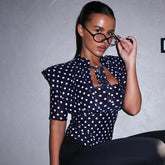 Woman wearing a navy blue polka dot blouse against a gray background