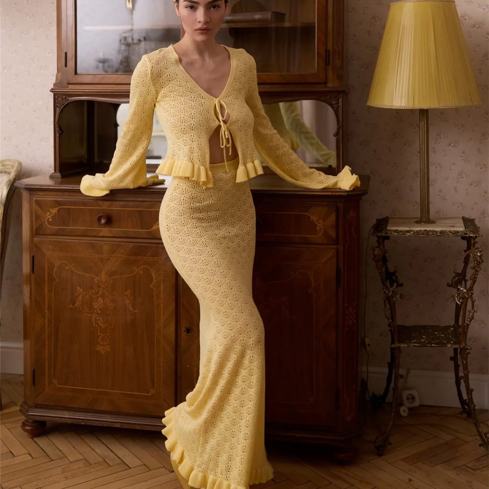 Woman in a yellow dress standing in an elegant room with wooden furniture and a lamp.