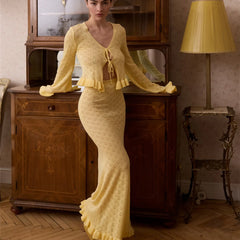 Woman in a yellow dress standing in an elegant room with wooden furniture and a lamp.