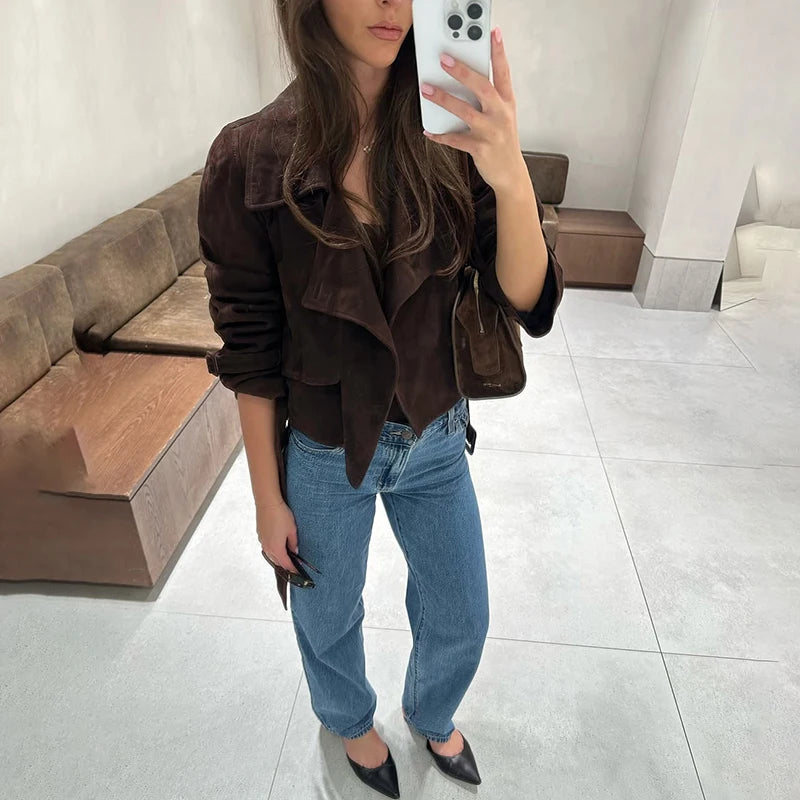 Person wearing a brown jacket and blue jeans taking a mirror selfie.