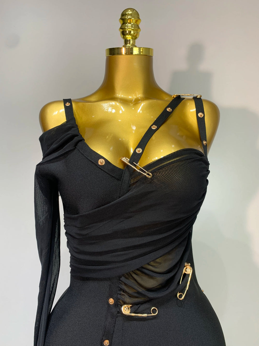 Black dress with gold accents on a mannequin against a neutral background