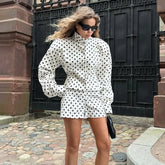 Woman in a polka dot outfit standing outdoors near a black gate.
