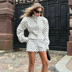 Woman in a polka dot outfit standing outdoors near a black gate.