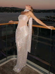 Woman in a sparkling silver gown standing on a balcony overlooking water at dusk.
