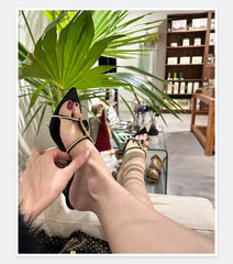 Person wearing high-heeled shoes with decorative elements, sitting in a room with plants and furniture.