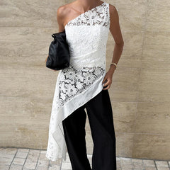 Person wearing a white one-shoulder lace dress with black pants against a beige wall.