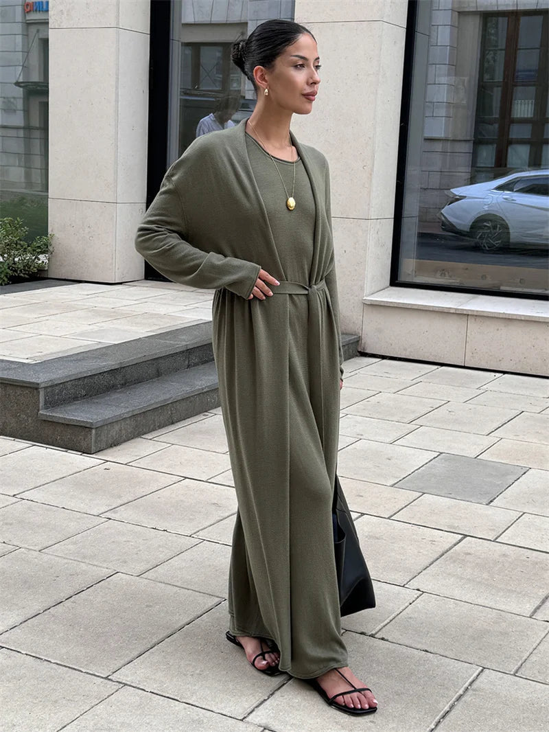 Woman in a long olive green dress standing on a sidewalk.