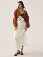 Woman wearing a rust-colored cardigan over a white dress with a bow on a white background