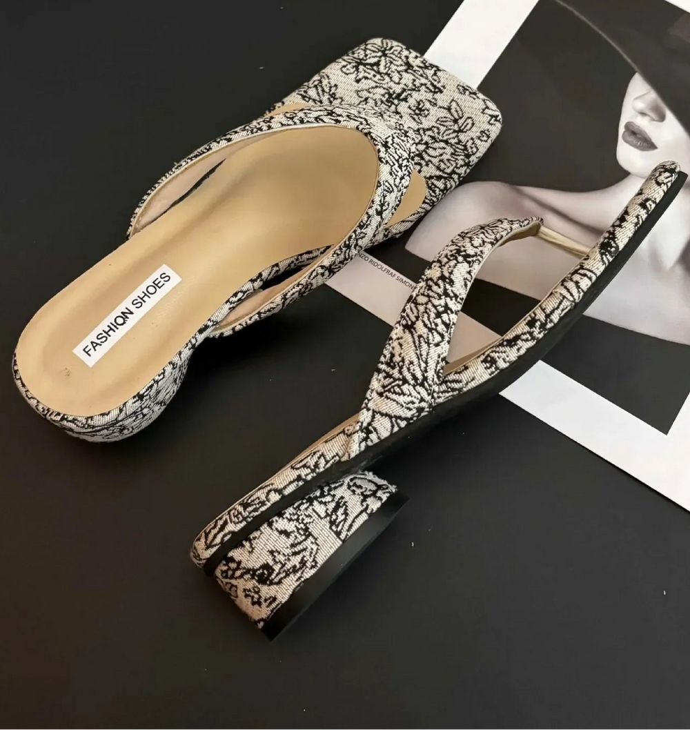 Pair of floral-patterned sandals on a dark surface with a magazine underneath.