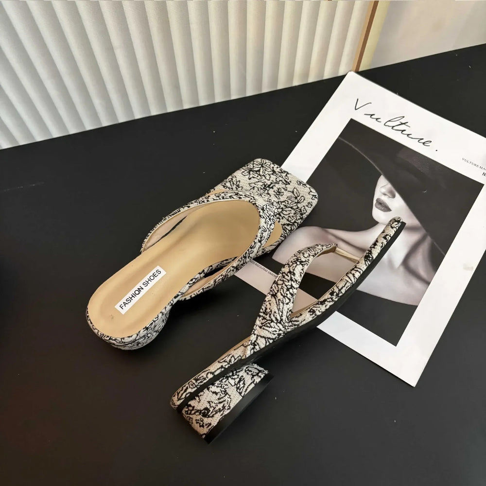 Pair of floral-patterned sandals on a dark surface with a magazine underneath.