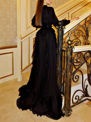 Woman in a black evening gown standing on a staircase with ornate railings.