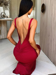 Woman in a red dress with an open back, sitting on a light-colored floor.