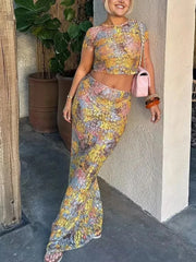 Woman in a floral outfit standing against a wall with plants in the background
