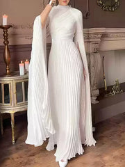 Woman wearing a white pleated dress in an elegant room with candles and decorative elements.