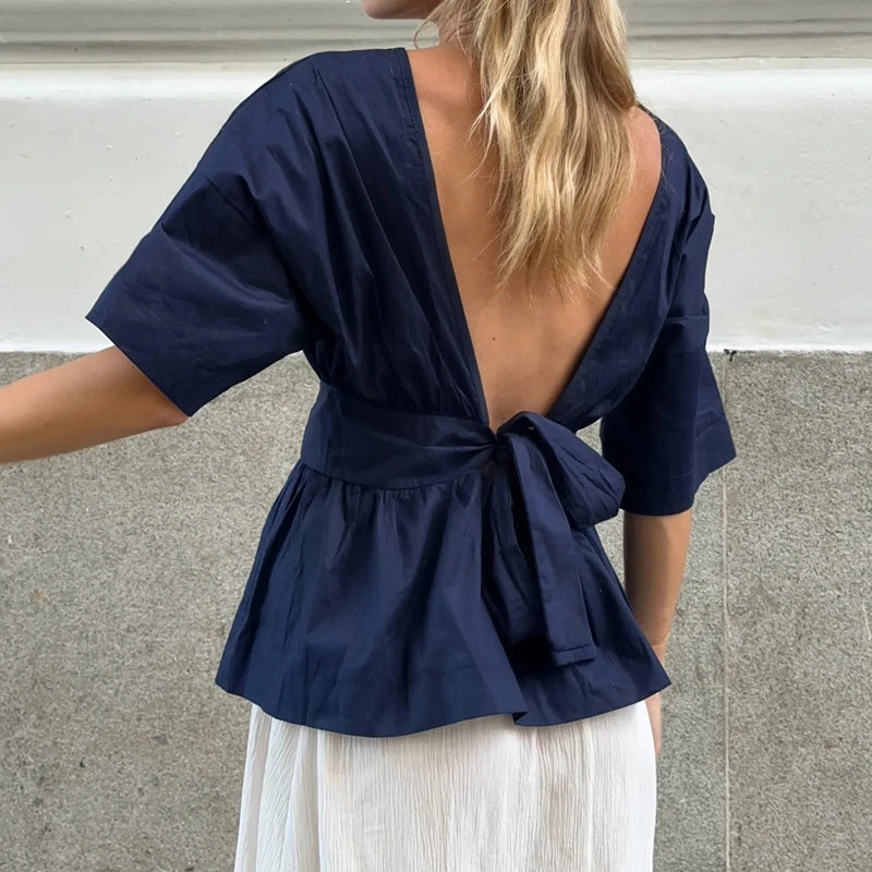 Navy blue top with open back worn by a person, standing against a neutral background.