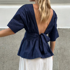 Navy blue top with open back worn by a person, standing against a neutral background.