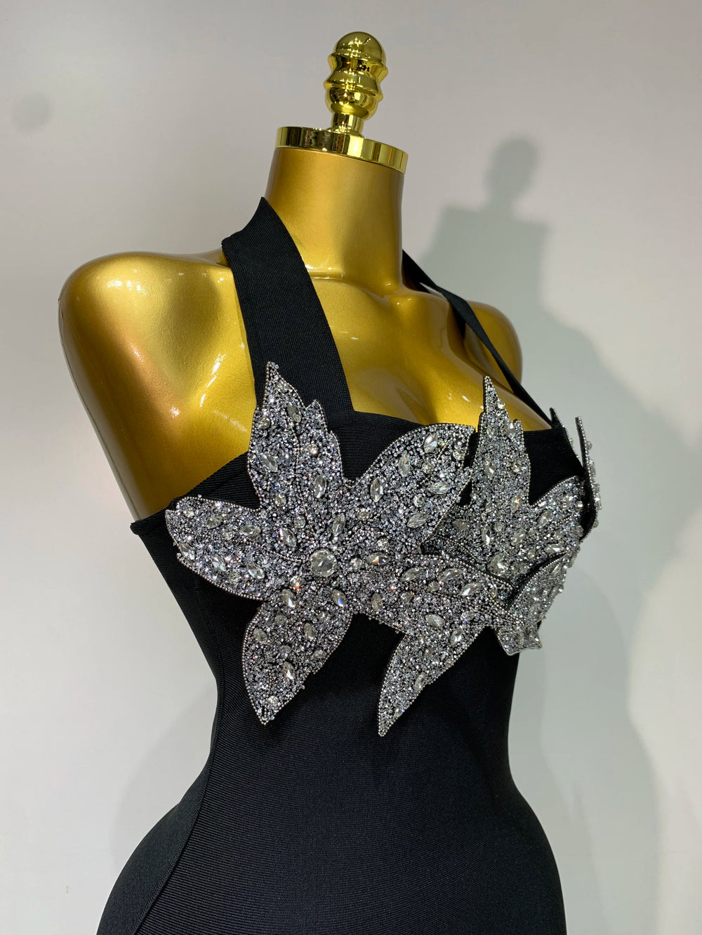 Black dress with silver floral embellishments on a gold mannequin against a white background