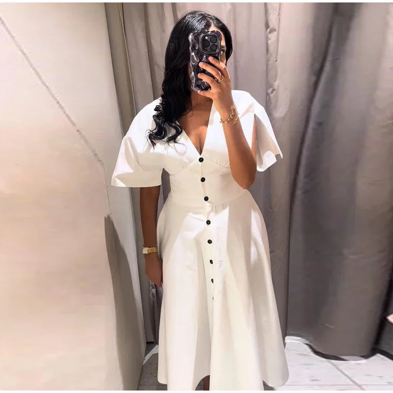 Person wearing a white dress with black buttons in a neutral setting