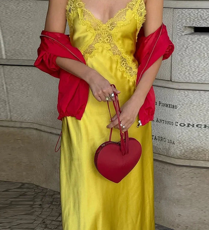Person wearing a yellow dress with red accents and holding a red heart-shaped handbag.