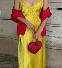 Person wearing a yellow dress with red accents and holding a red heart-shaped handbag.