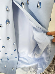 Close-up of a light blue fabric with embedded crystals, held by a hand.