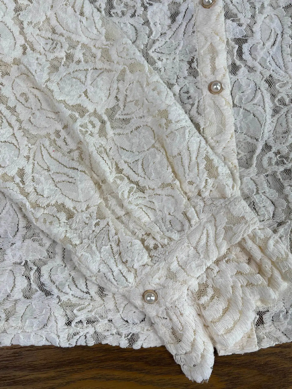 Close-up of a lace garment with button details on a wooden surface