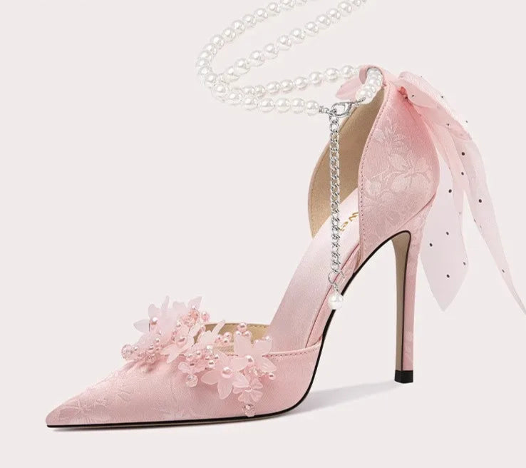 Pink high-heeled shoe with floral design and chain on a white background