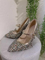 Pair of patterned high-heeled shoes on a light surface with greenery in the background