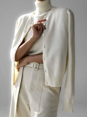 Person wearing a cream-colored cardigan over a turtleneck sweater and pants on a gray background