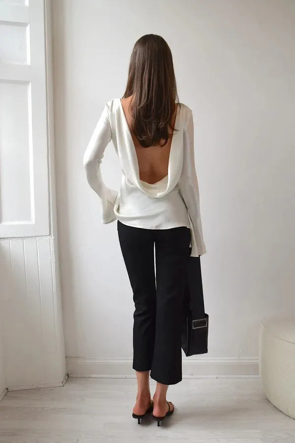 Woman wearing a white open-back top and black pants in a minimalistic room.