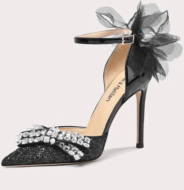 Black high-heeled shoe with decorative bow and flower on a white background