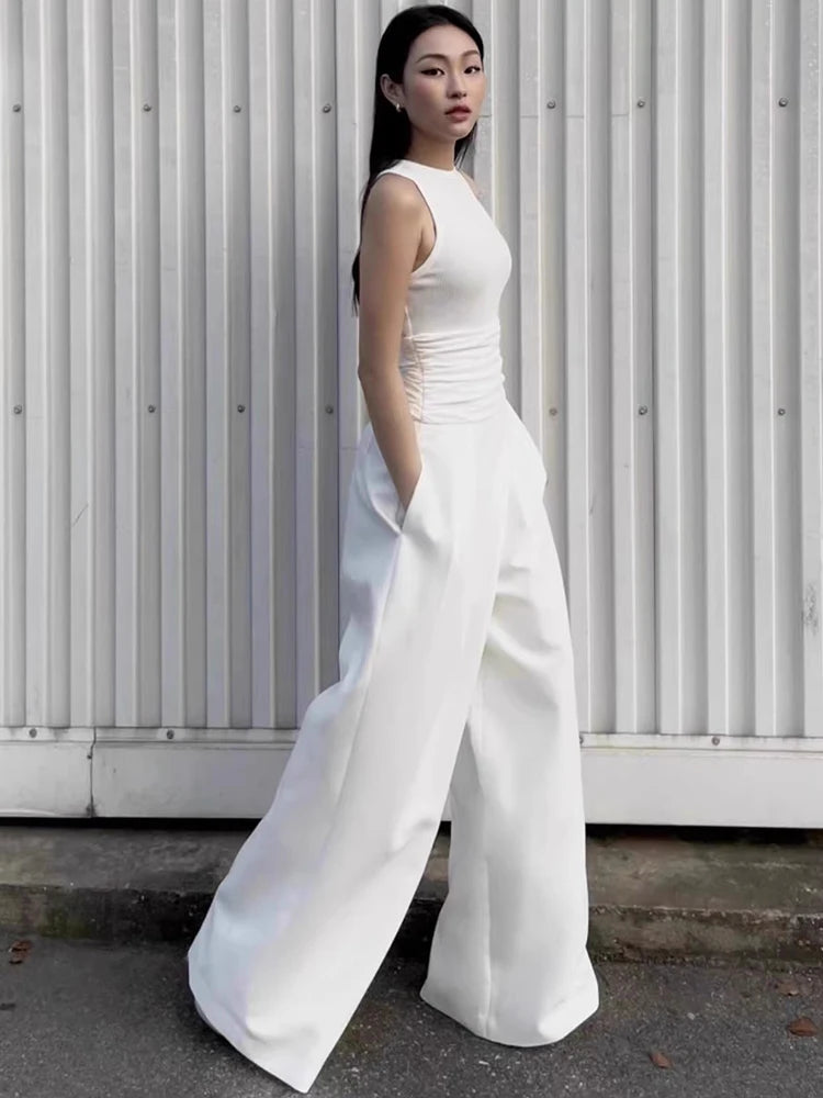 Woman wearing a white sleeveless jumpsuit against a white wall.