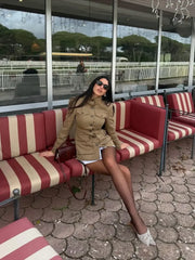 Woman sitting on a red and white striped bench in an outdoor setting with large windows in the background.