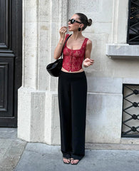 Woman wearing a red lace top and black wide-leg pants standing against a stone building.