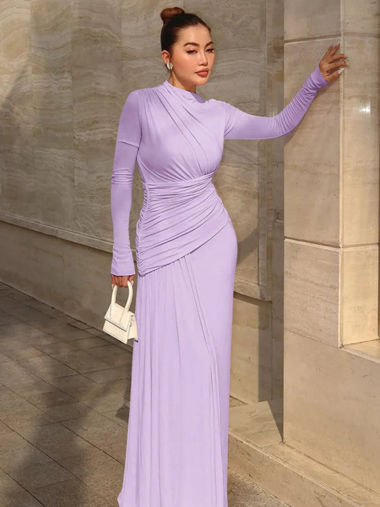 Woman in a long purple dress standing against a stone wall.