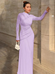 Woman in a long purple dress standing against a stone wall.