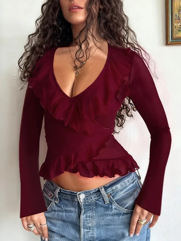 Woman wearing a burgundy ruffled top and blue jeans against a plain background