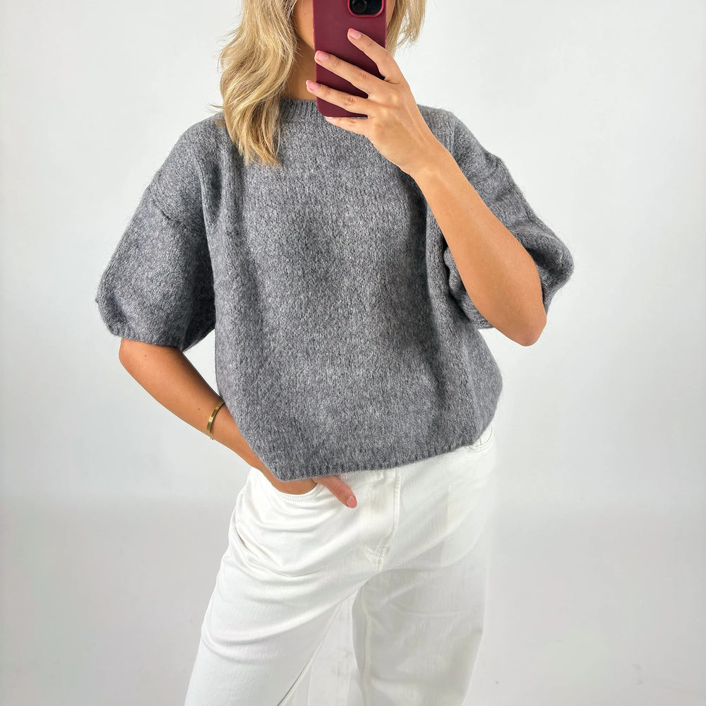 Person wearing a gray sweater and white pants against a plain background