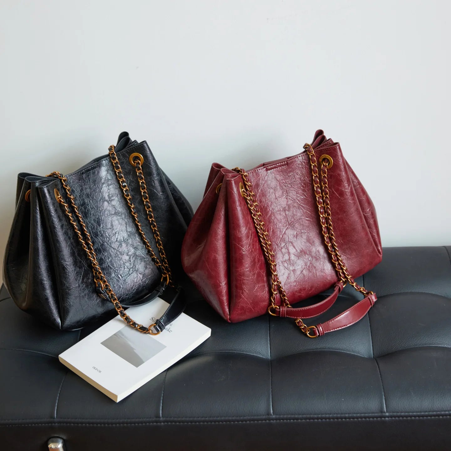 Two leather handbags, one black and one red, with gold chains on a dark surface.