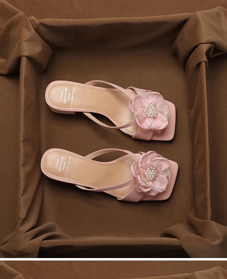 Pair of pink sandals with floral embellishments on a brown fabric background