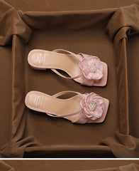 Pair of pink sandals with floral embellishments on a brown fabric background