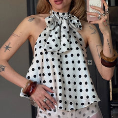 Woman wearing a polka dot dress with a large bow, taking a mirror selfie.