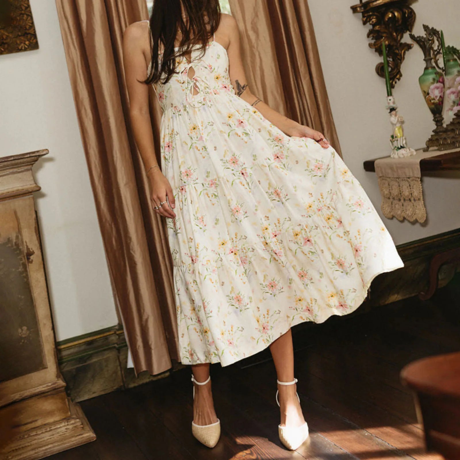 Woman wearing a floral dress in an indoor setting with curtains and decorative items.