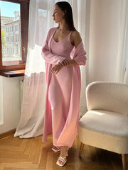 Woman in a pink dress standing by a window with white curtains.