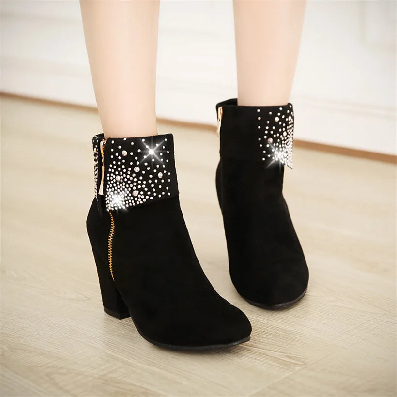 Black ankle boots with rhinestone details on a light wooden floor.