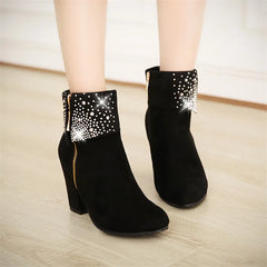 Black ankle boots with rhinestone details on a light wooden floor.